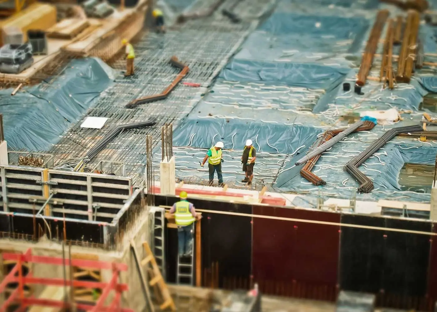 Construction workers lay rebar and concrete forms on a large building foundation.