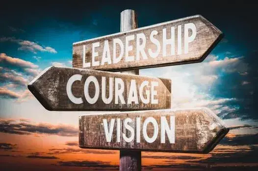 Directional signpost with Leadership, Courage, and Vision against a dramatic sky.