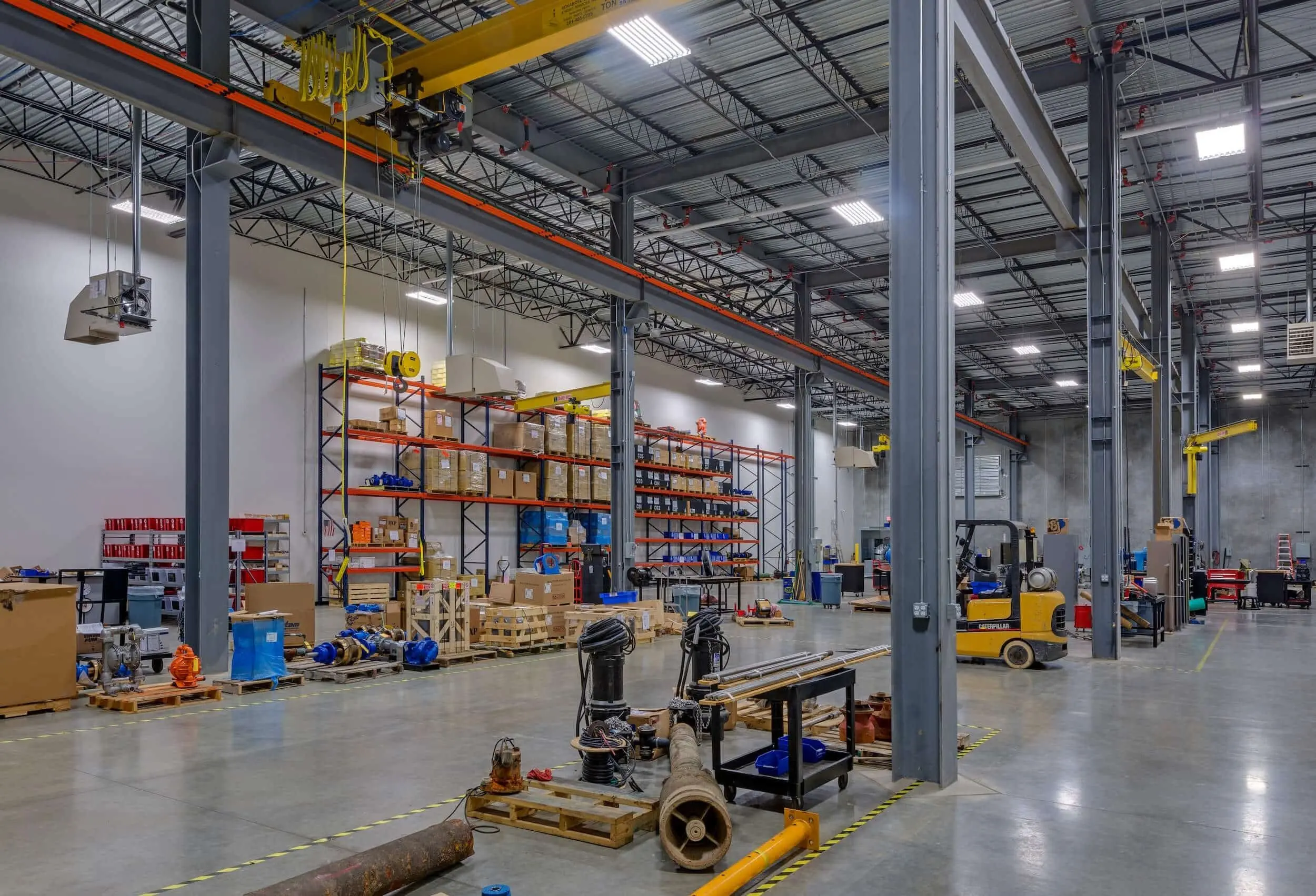 Spacious industrial warehouse with storage shelves, yellow overhead cranes, and a forklift.