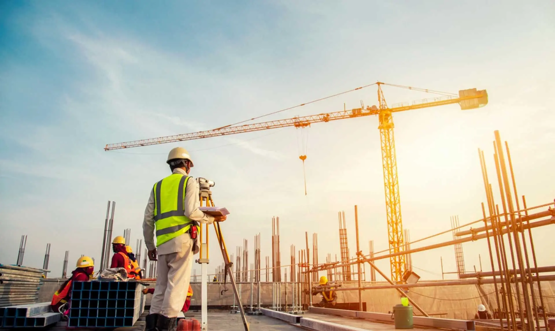 Construction worker surveying a building site with a large crane at sunrise or sunset.